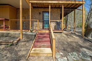 Stroll up the wooden staircase to a charming stone building surrounded by lush trees and natural elements.