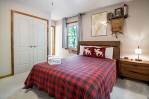 A bedroom with a bed, a nightstand, a lamp, a window with curtains, a map on the wall, and a door.