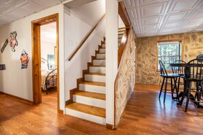 Eine hölzerne Treppe führt zu einer zweiten Etage, einem Essbereich mit einer Steinwand und einem Bett mit einer gestreiften Decke.