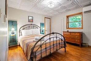 Ein Schlafzimmer mit Bett, Kommode, Fenster und einer Decke mit Lampenleuchte.