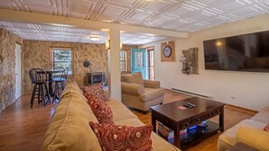 A spacious living room with a stone wall, a fireplace, a large TV, and a dining area with chairs and a table.
