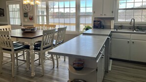 Una cucina con mobili bianchi, un'area pranzo con tavolo e sedie in legno, e ampie finestre con vista su un corpo d'acqua.