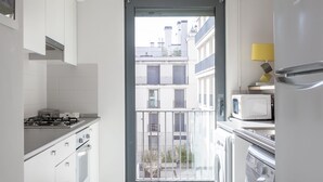 A modern kitchen with a gas stove, oven, microwave, and a built-in washing machine. A sliding glass door leads to a balcony with a view of buildings. - Vita Portucale | Downtown Premium with Garage (Lisboa)