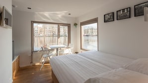 Une chambre avec un grand lit, un bureau et une chaise près d’une fenêtre donnant sur un canal.