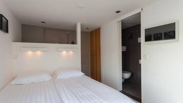 A bedroom with two beds, a wooden wardrobe, a bathroom with a toilet and shower, and a small shelf with pictures.