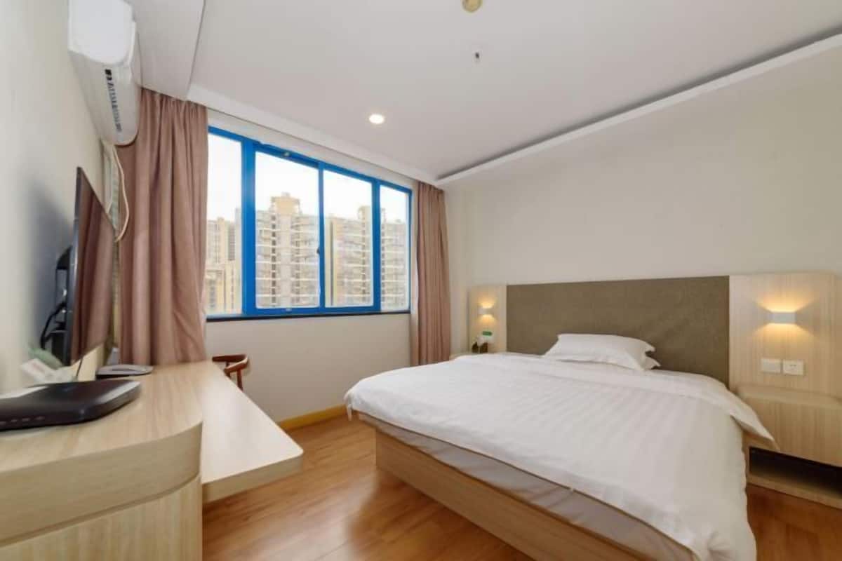 A hotel room with a bed, a desk, a chair, a TV, and a window with a city view.