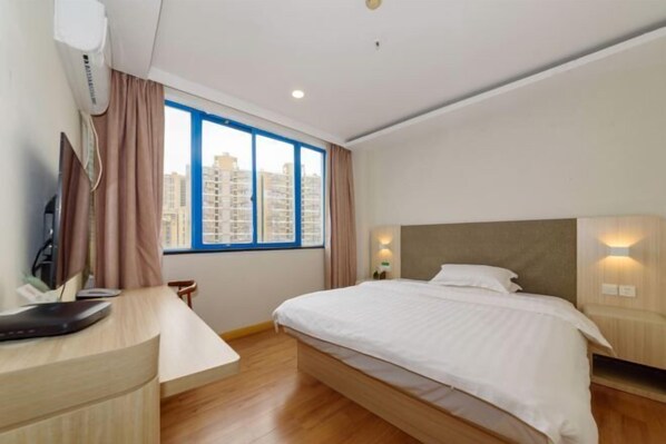 Ein Hotelzimmer mit Bett, Schreibtisch, Stuhl, Fernseher und einem Fenster mit Blick auf die Stadt.