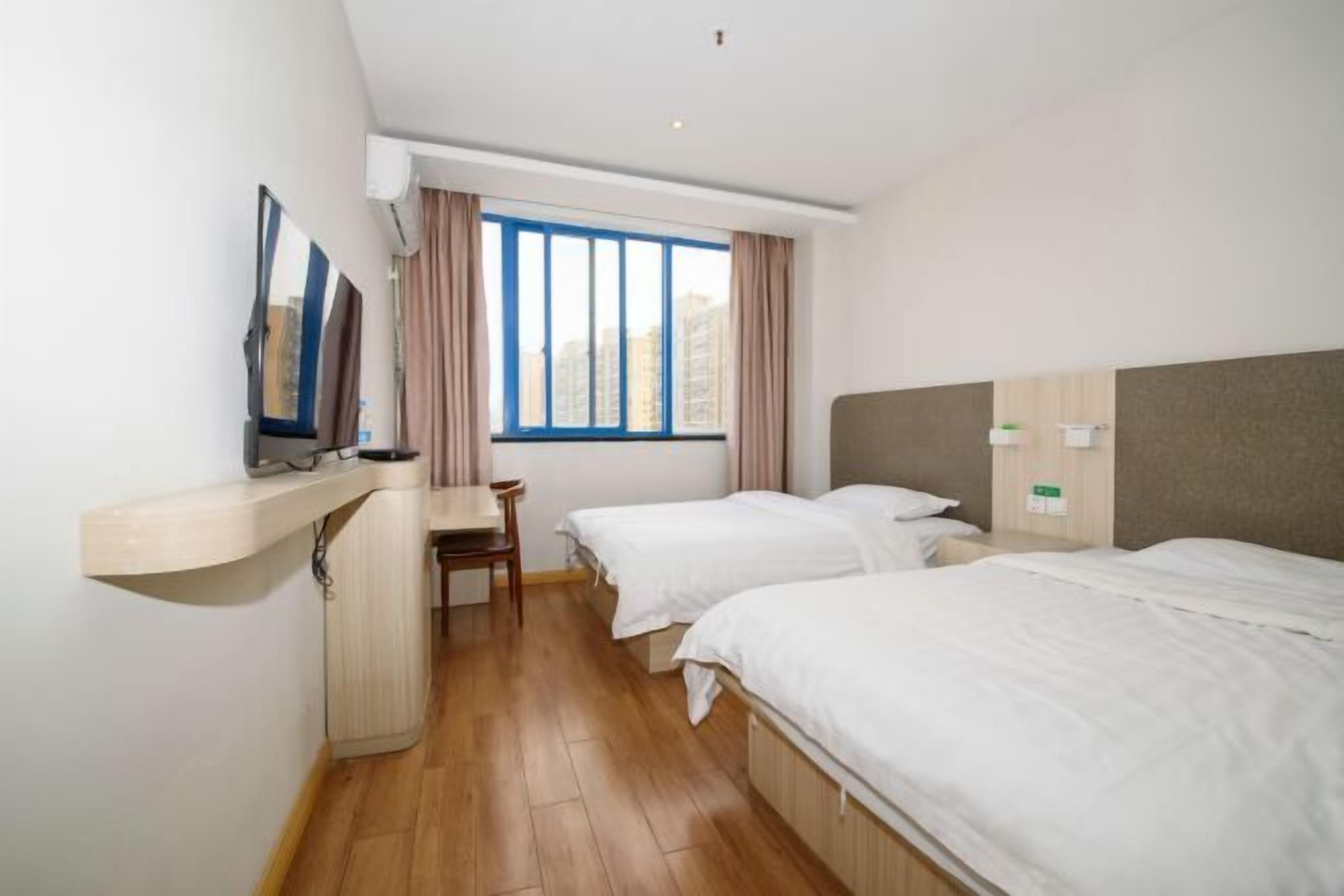 A hotel room with two single beds, a desk, a chair, and a large window with curtains.