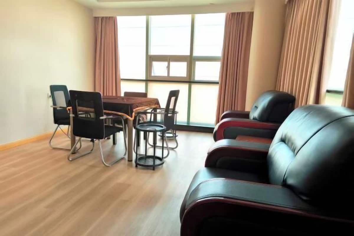 A room with a dining table, chairs, a sofa, and large windows with curtains.