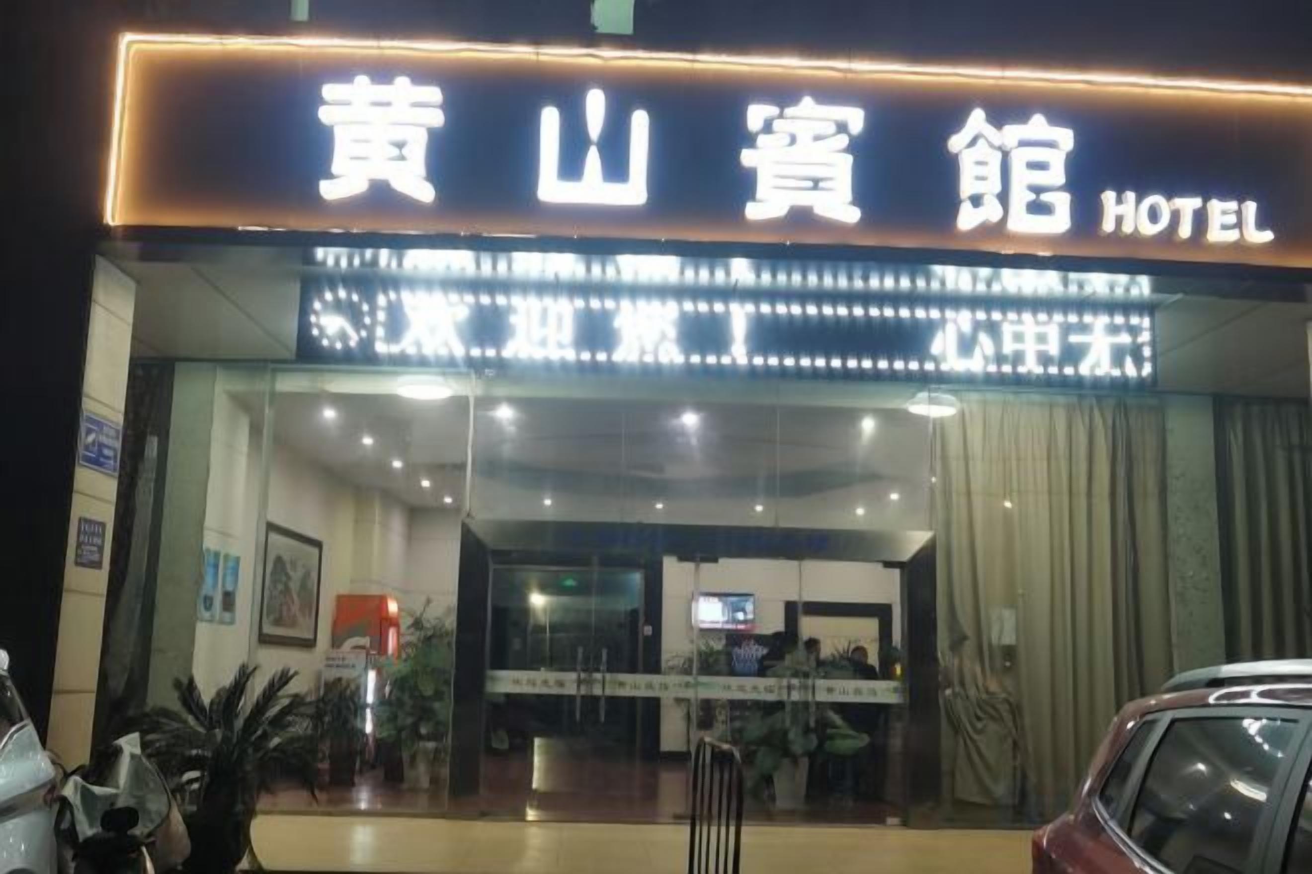 A hotel entrance with a sign in a foreign language, a reception desk, and a car parked outside.