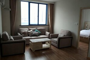 Ein Wohnzimmer mit einer Couch, zwei Sesseln, einem Couchtisch und einem großen Fenster mit Vorhängen.
