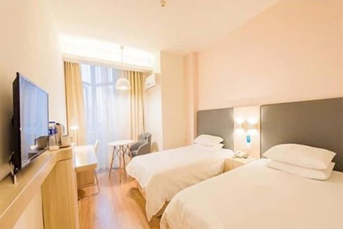 A hotel room with two beds, a desk, a chair, a TV, and a window with curtains.