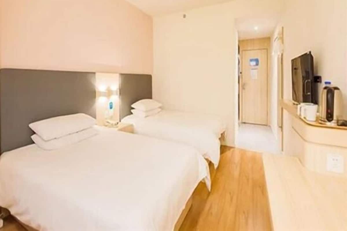 A hotel room with two beds, a bedside table with a lamp, a television, and a coffee maker.