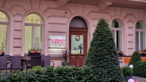 Fachada de un hotel con el nombre 'IRIS' y un cartel que indica que es un hotel y spa. Hay plantas en macetas y un árbol de Navidad al frente.