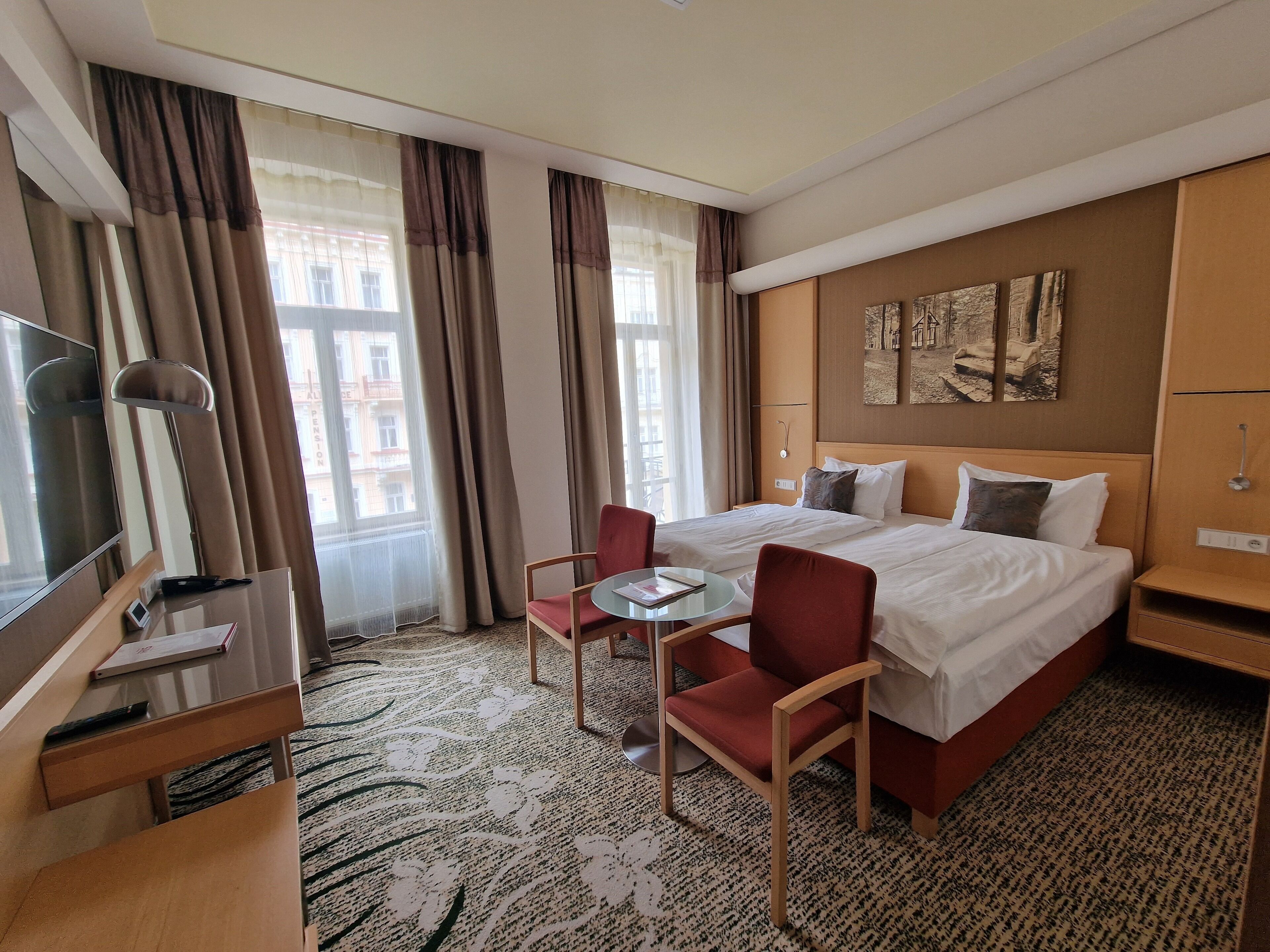 Een hotelkamer met een bed, een bureau, een stoel, een televisie en een raam met gordijnen.