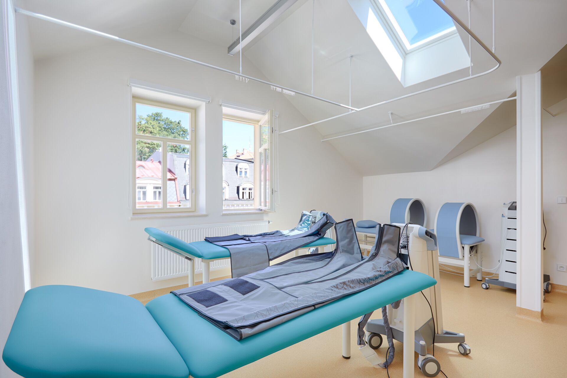Une salle d’examen médical équipée d’un lit pour les patients, d’une table d’examen et d’une fenêtre donnant sur les bâtiments environnants.