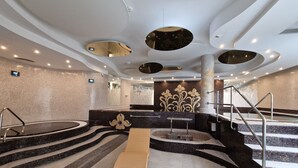 Un spa moderno con un jacuzzi central, varios niveles de escalones y una zona de descanso.