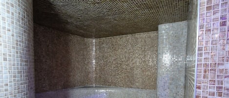 A tiled shower with a curved bench and a drain in the center.