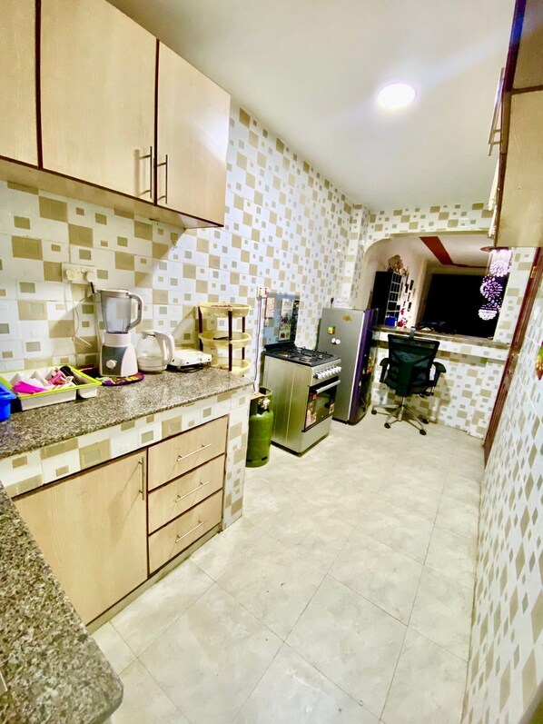 Una cocina compacta con armarios de madera, estufa a gas, refrigerador y un pequeño comedor con una silla.