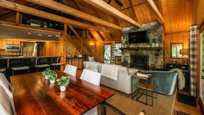 A rustic cabin interior with a wooden dining table, white sofa, and stone fireplace. - Beautiful view with firepit and hot tub. Only 7 minutes to Cashiers and Glenville! (Cashiers)