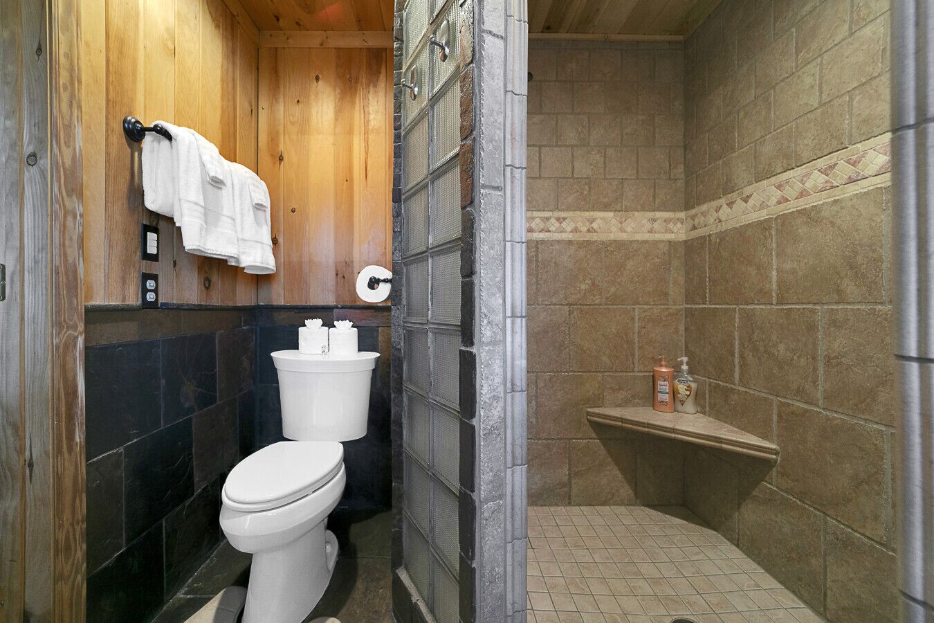 A compact bathroom with a toilet, a towel rack, a shower area, and a small shelf with toiletries.