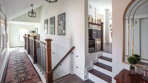 Un pasillo amplio con una escalera de madera, un tapete estampado y cuadros enmarcados en la pared.