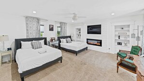 Habitación de hotel con dos camas, televisión, chimenea y una zona de estar con una silla y una mesa.
