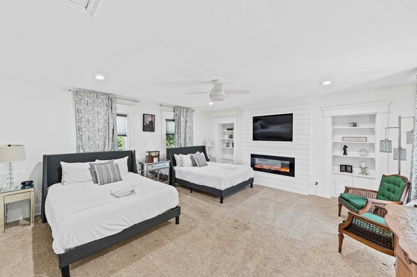 A hotel room with two beds, a TV, a fireplace, and a seating area with a chair and table. - Gather Together - Home for 20 - Pool AND Hot Tub! (Williamstown)