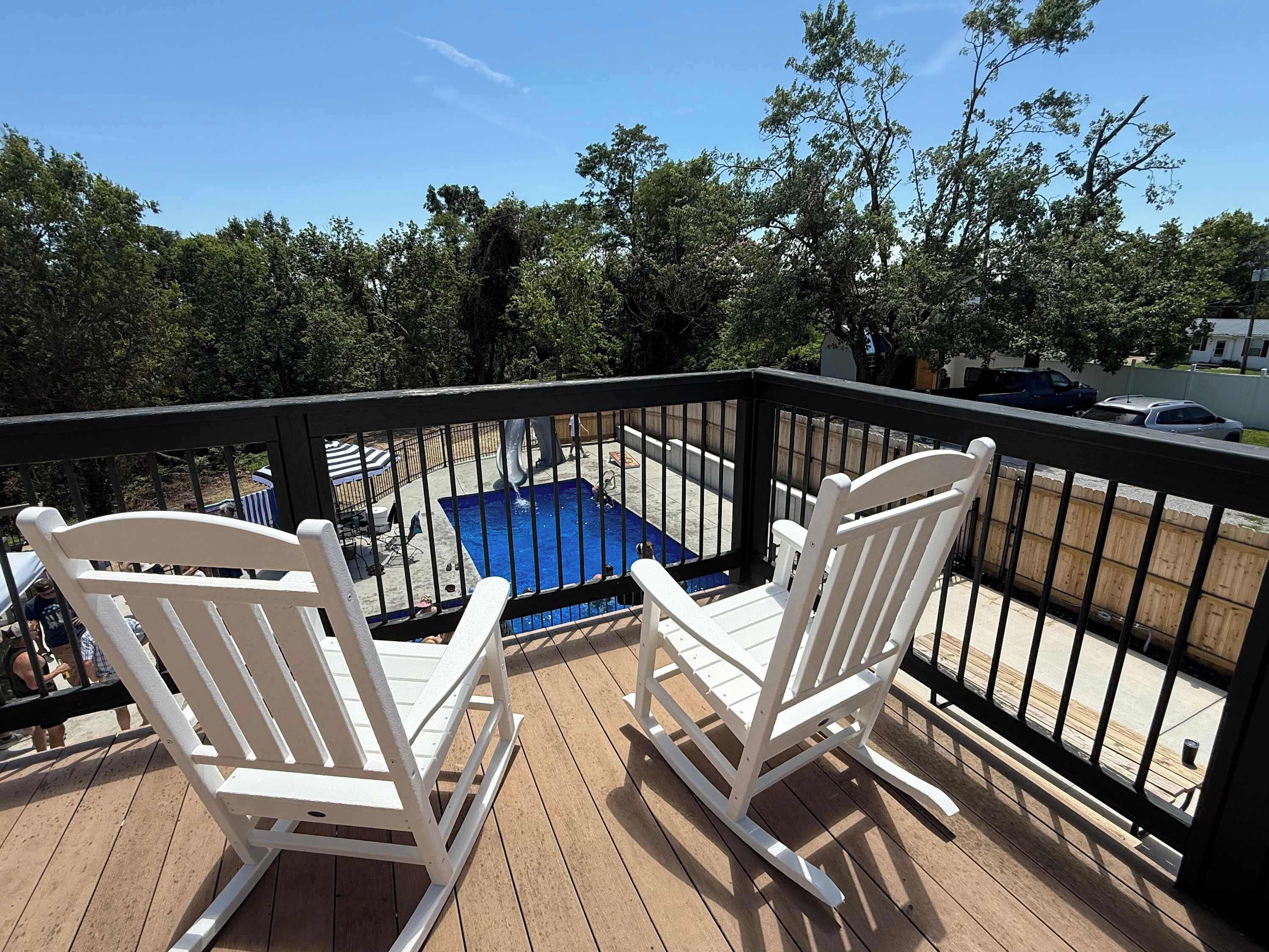 A wooden deck with white rocking chairs overlooking a swimming pool.