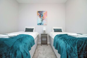 A twin room with two beds, a small bedside table with a lamp, and a colorful abstract painting on the wall.