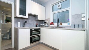 Une cuisine moderne avec des meubles blancs, un four encastré, une bouilloire et une fenêtre donnant sur un beau paysage.
