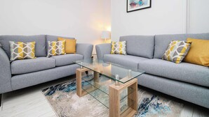 Un salon moderne avec deux canapés gris, une table basse en verre et des coussins à motifs.