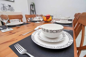 A dining table set with plates, bowls, and cutlery, with a bowl of fruit and glasses on the table.
