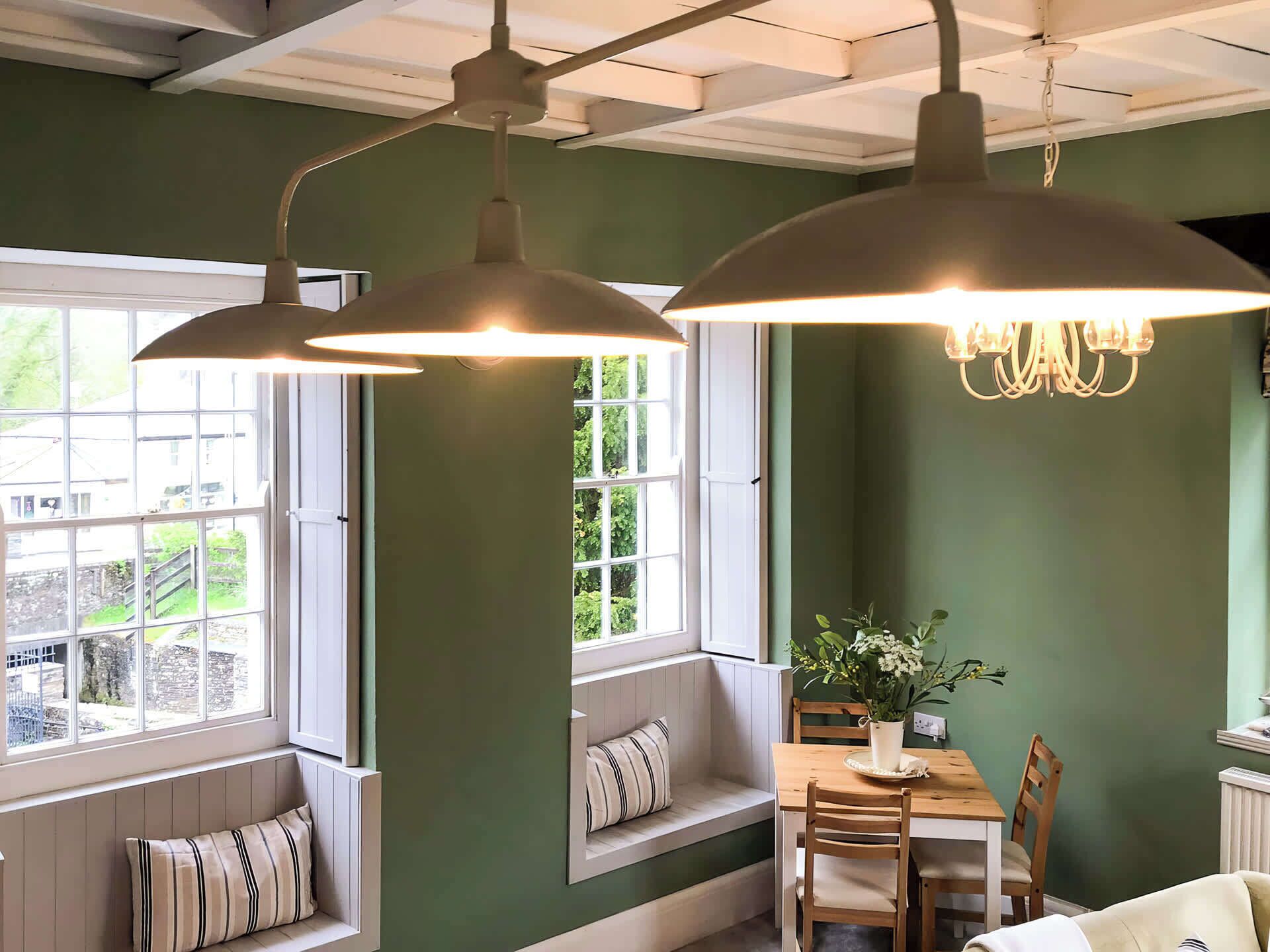 A room with a large window, a dining table with chairs, a bench with cushions, and a chandelier.