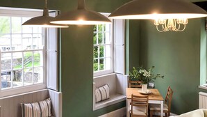 A room with a large window, a dining table with chairs, a bench with cushions, and a chandelier. - The Cornish Peak: Cornwall by STAE-Homes (Cornwall)