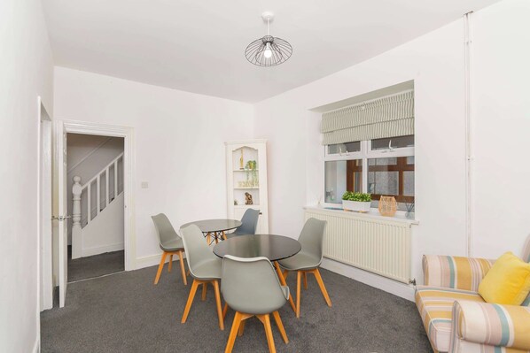 Un espace de vie compact comprenant un coin repas, un canapé, un radiateur et une fenêtre avec des rideaux.