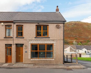 A two-story building with a brick facade, a large window on the ground floor, and a door with a sign above it. - THE SPACE Large House In Afan Forest Bike Park (Port Talbot)