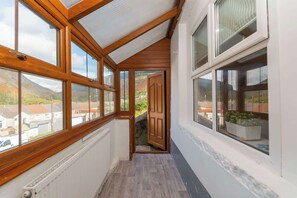 Un couloir étroit, avec des poutres en bois et de grandes fenêtres, qui mène à une porte.