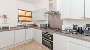 A modern kitchen with white cabinets, a stainless steel range hood, a built-in oven, and a window with a view. - THE SPACE Large House In Afan Forest Bike Park (Port Talbot)