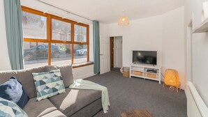 A living room with a sofa, television, and a window with curtains. - THE SPACE Large House In Afan Forest Bike Park (Port Talbot)