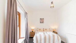 A bedroom with a bed, bedside lamps, a window with curtains, a radiator, and a wall-mounted light fixture. - THE SPACE Large House In Afan Forest Bike Park (Port Talbot)