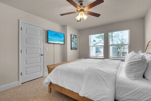 Quarto com cama de madeira, ventilador de teto, TV na parede e janela com persianas.