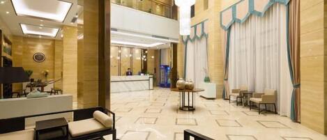 Un vestíbulo de hotel con una recepción, zona de estar y una escalera que lleva a un nivel superior.