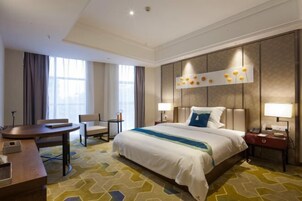 Una habitación de hotel con una cama grande, un escritorio, una silla y una mesita de noche con lámpara.
