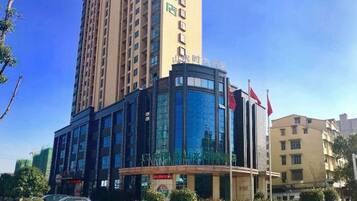 A modern hotel with a curved glass facade, a flagpole, and a parking lot with cars.