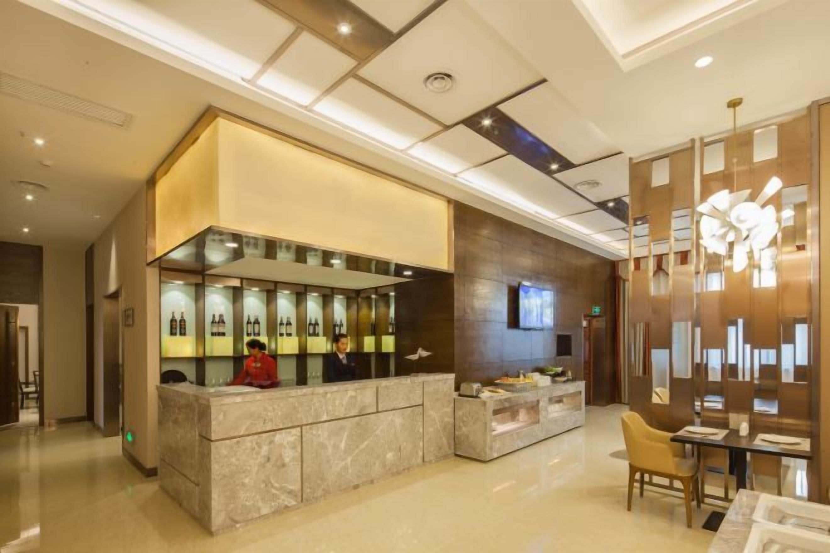 A hotel lobby with a reception desk, seating area, and a decorative wall.
