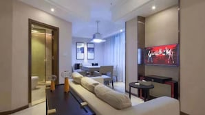 Ein modernes Hotelzimmer mit Sofa, Fernseher, Essbereich und Badezimmer.