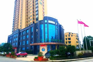 Un hotel de varios pisos con fachada de vidrio curvo, entrada central e izada de bandera.