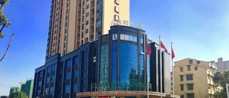 A multi-story building with a curved glass facade, a flagpole, and a sign indicating a hotel or similar establishment.