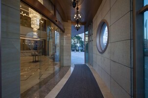 A corridor with a glass storefront on the left, a circular window on the right, and a black mat leading to an outdoor area.
